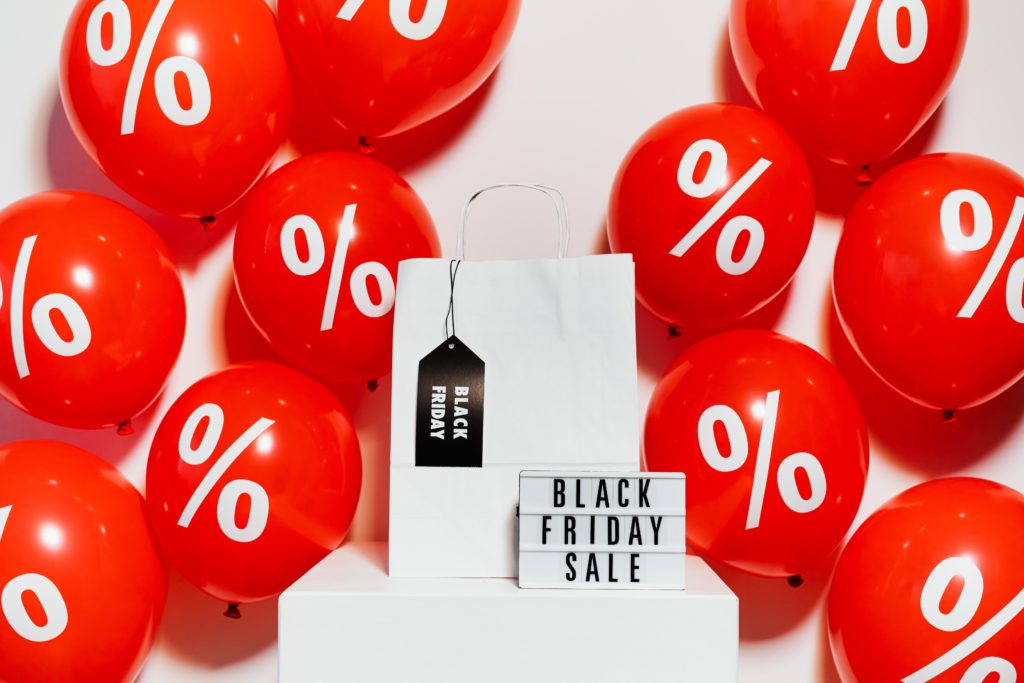 Red balloons surrounding white bag and sigh that read black Friday deals.