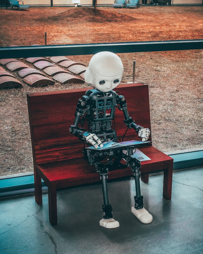 A robot child sits at a bench and uses a mobile device. Photo by Andrea De Santis on Unsplash