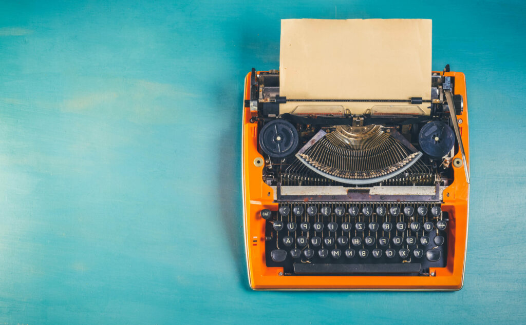 Workspace with orange vintage typewriter on blue wooden table background, toned